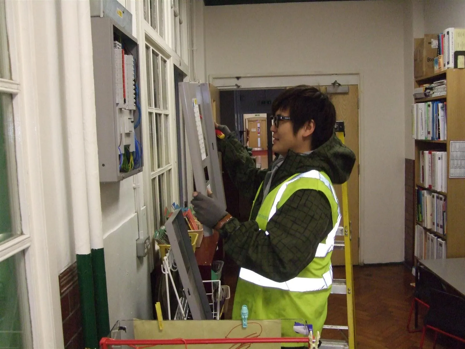 Electrician refitting a fuse board cover at a school in East London