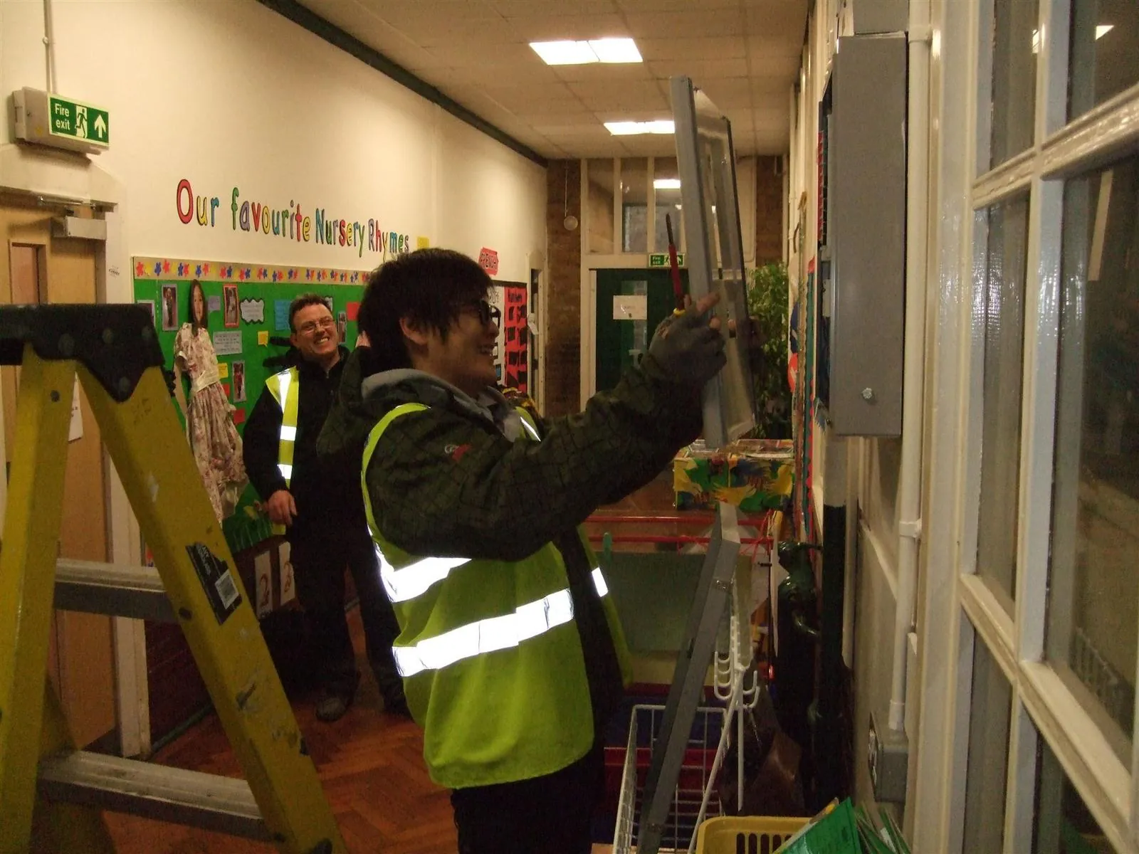 Electricians upgrading a fuse board in a school corridor in East London